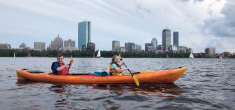 Two people on a kayak on the Charles River with the city in the background