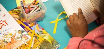 child reading a book at a desk with crayons and pencils