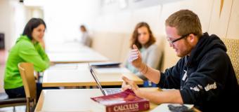 three students sit at tables with a calculus textbook and calculator