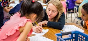 female teacher helping young students at desk
