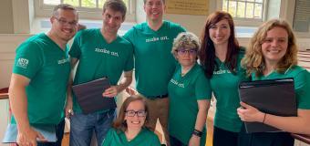 Group of people sitting in or standing around pews wearing green shirts that say "Make Art"