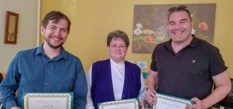 Chris Clark, Kate Hendrix and Josh Baldwin stand in a row and smile while holding their awards.