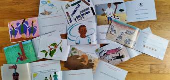Multiple books lay open on a wooden floor, each with a different artworks depicting children or plants.