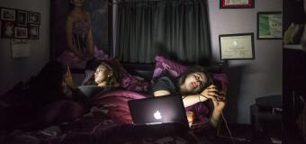 young people look at their phones in a dark room while laying in bed