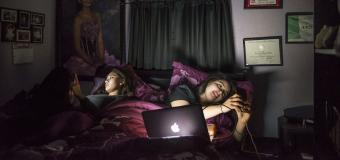 young people look at their phones in a dark room while laying in bed