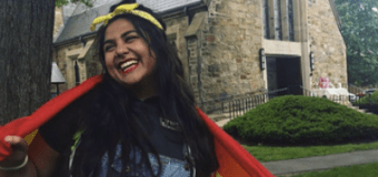 Seana standing outside on the quad with a pride flag around her shoulders