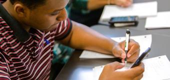 student using calculator on cell phone while writing on a piece of paper