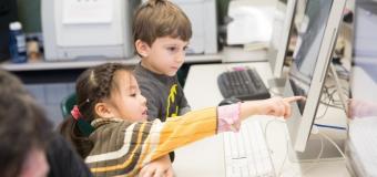 Two students sitting at a computer while one points to the screen.