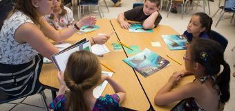 A group of students sitting at a table reading books with a teacher
