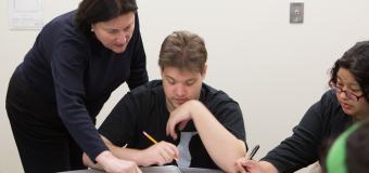 threshold student writing in class and receiving assistance from the teacher