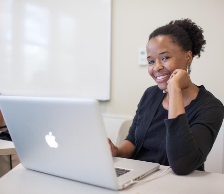 student smiling from behind her laptop