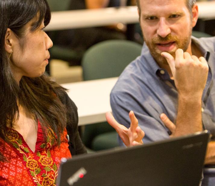 In a classroom, a woman explains something to a male classmate.