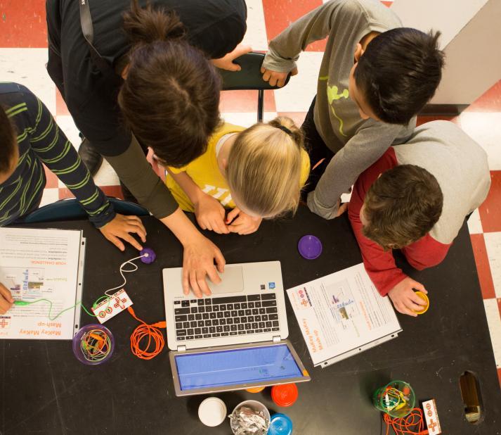 overhead view of children and teacher at table working with laptop and notebooks