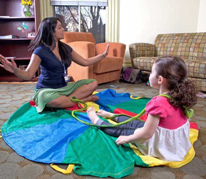 female expressive therapist sitting with small child on a parachute engaging her in play therapy