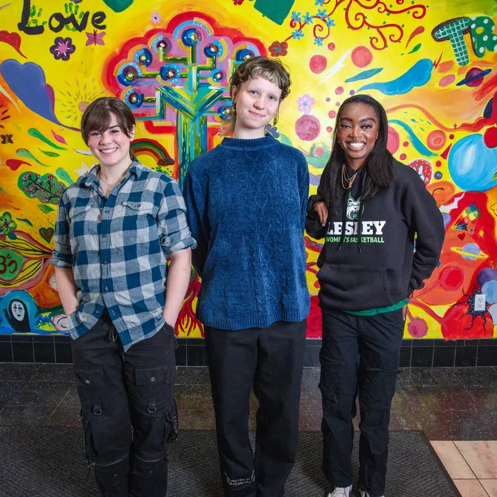 Three Lesley students standing in front of the art mural in University Hall