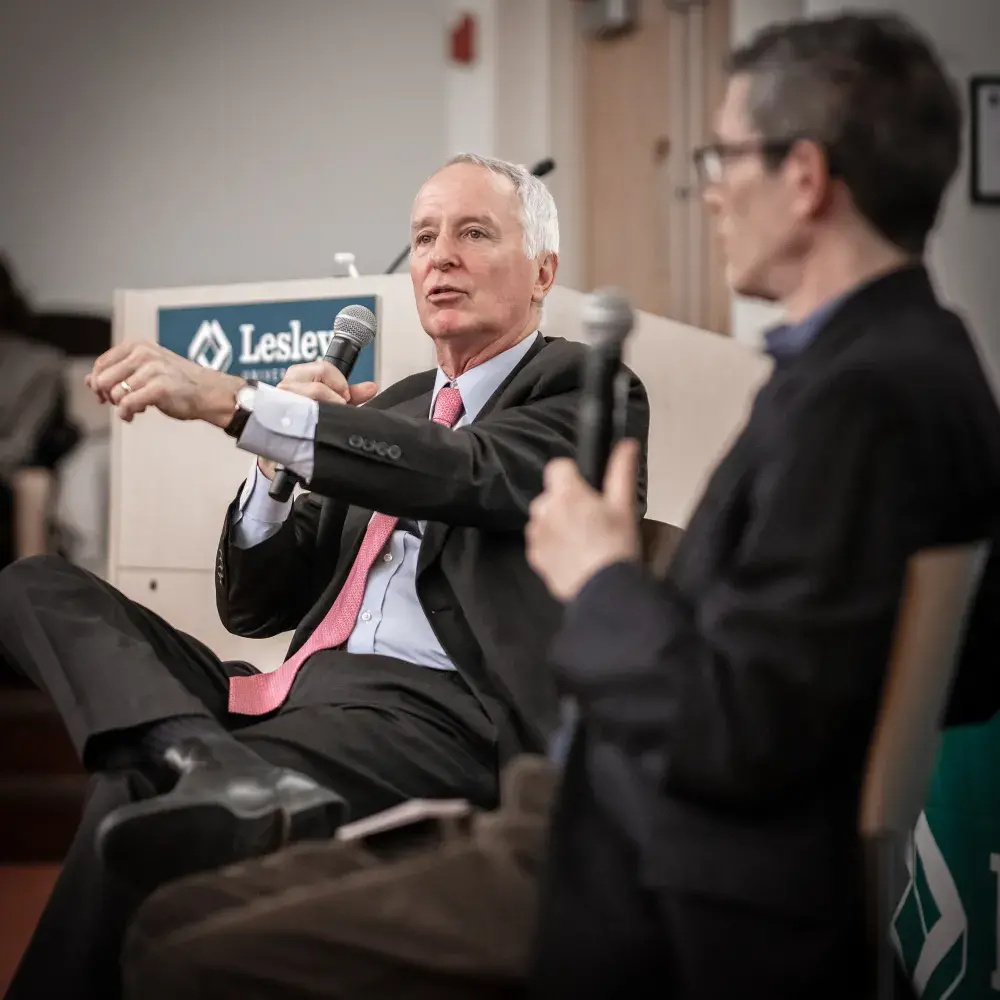 Two people sit side by side, each in suits and holding microphones