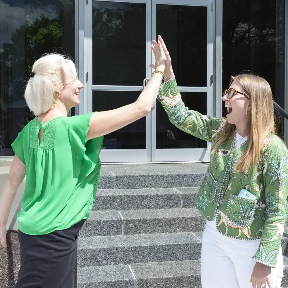 two women high-fiving outside in front of stairs and doorway