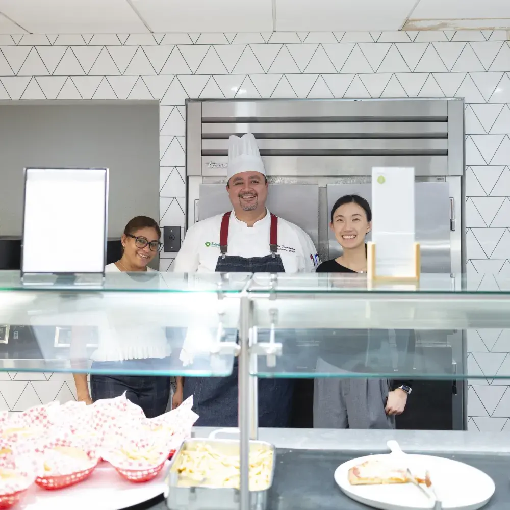 Chef and two dining workers behind a food case