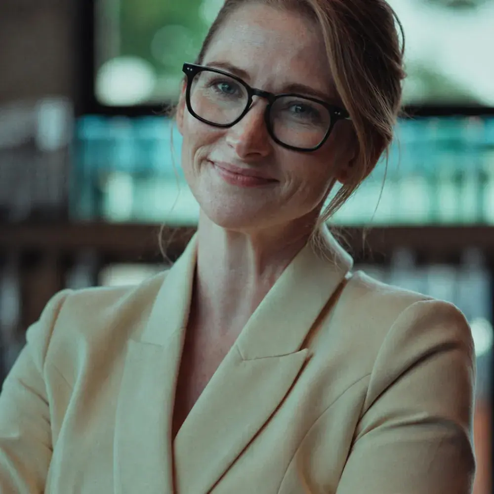 Laura in beige blazer and black glasses smiling