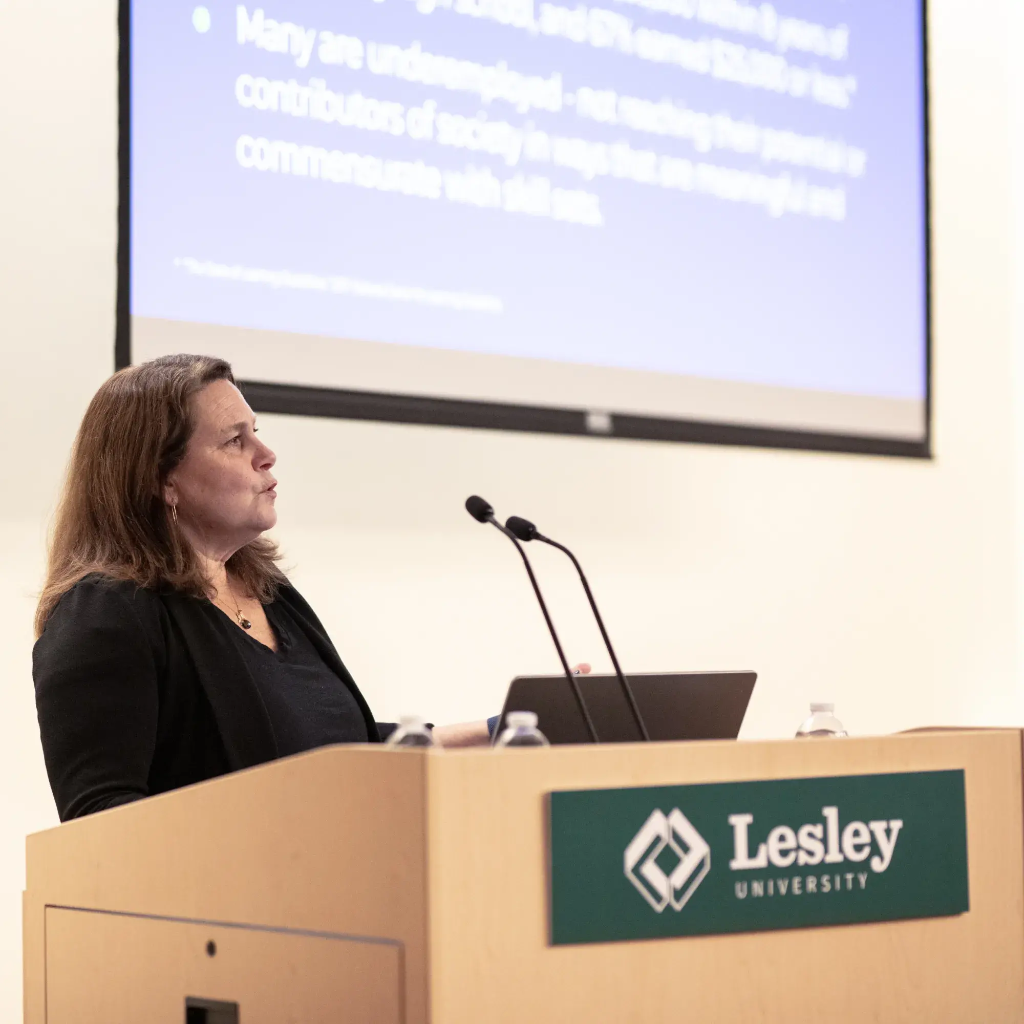 Carolyn Jeppsen at podium in front of slide show