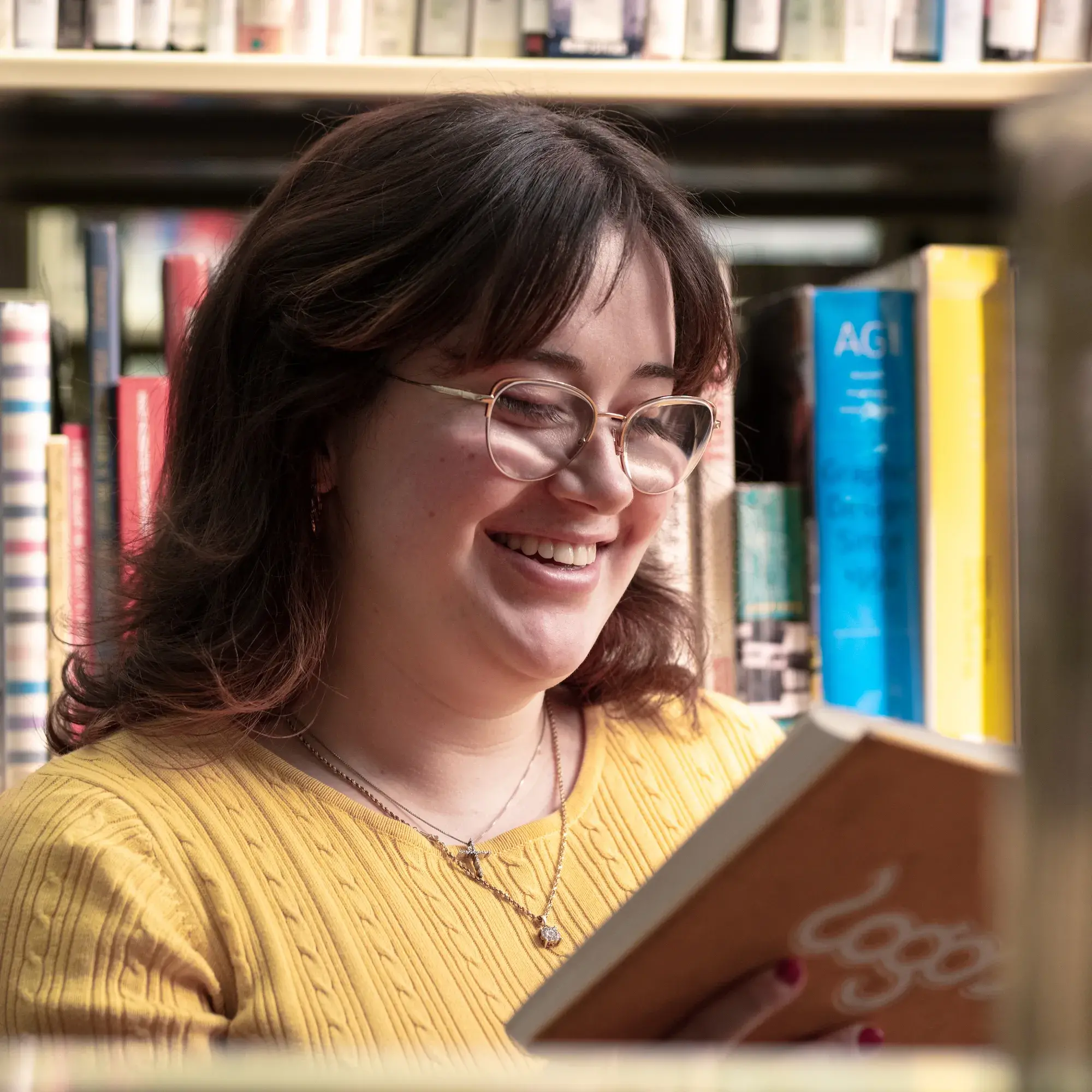 Margaret sitting in front of bookcase smiling and reading