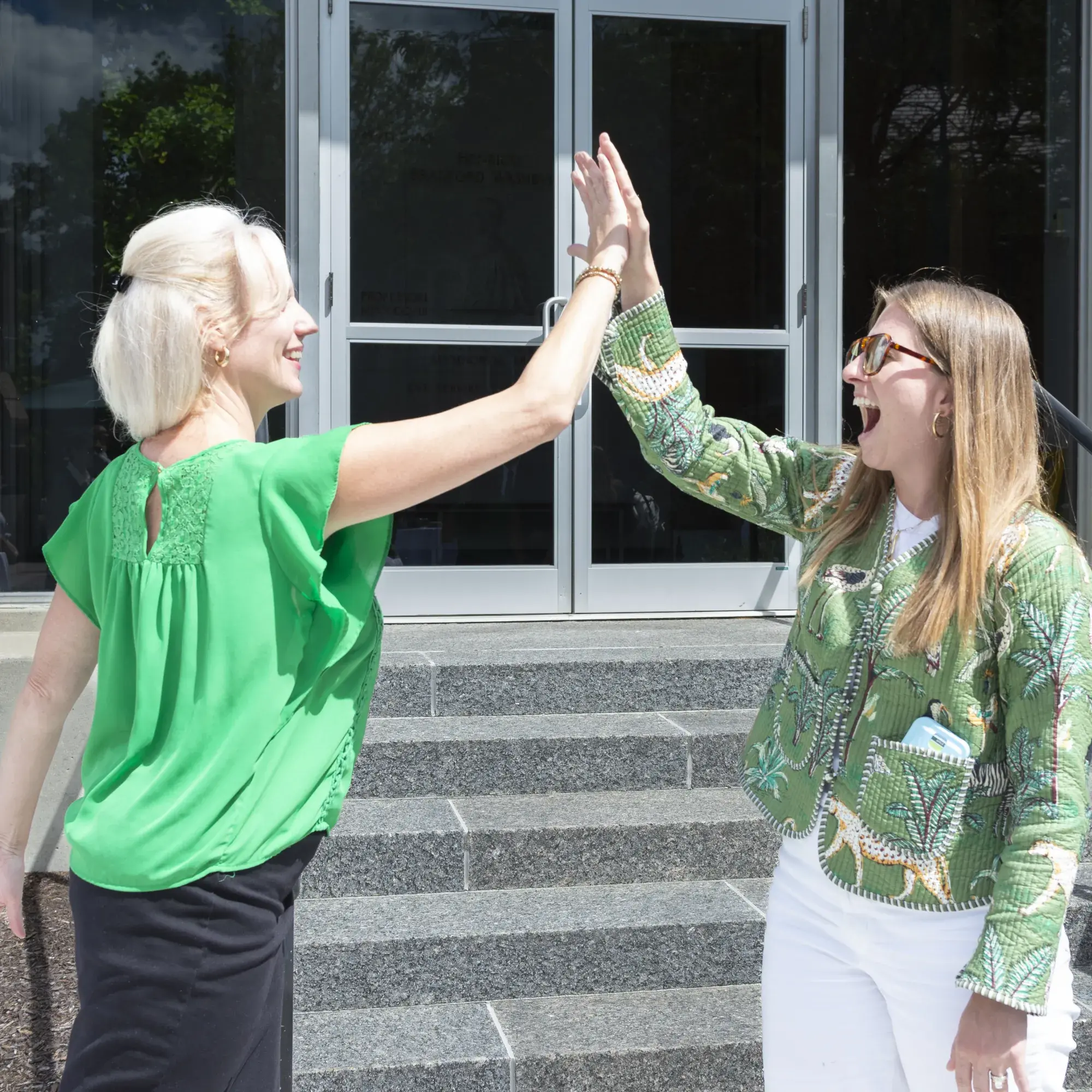 two women high-fiving outside in front of stairs and doorway