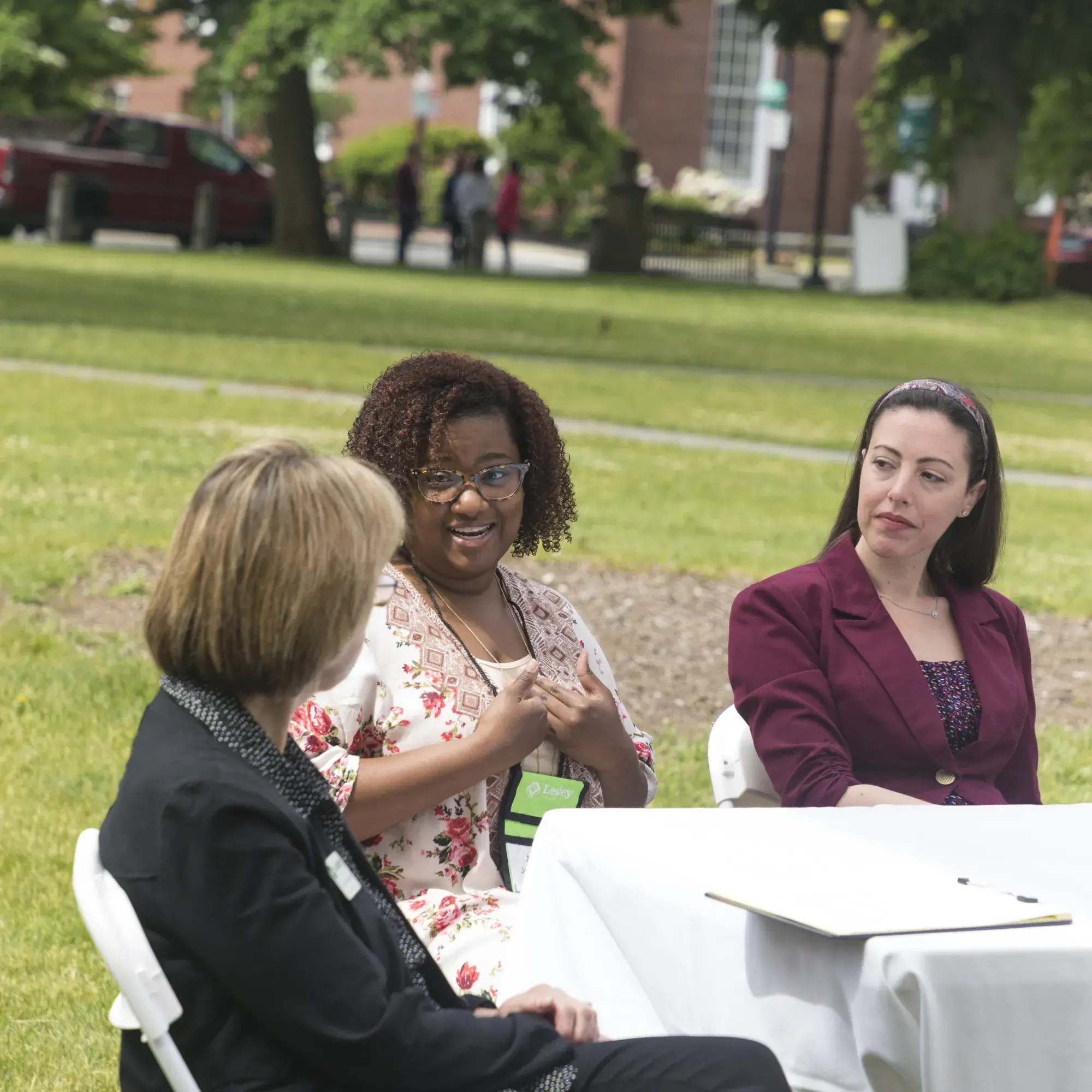 Three people sitting at a table outside talking to each other