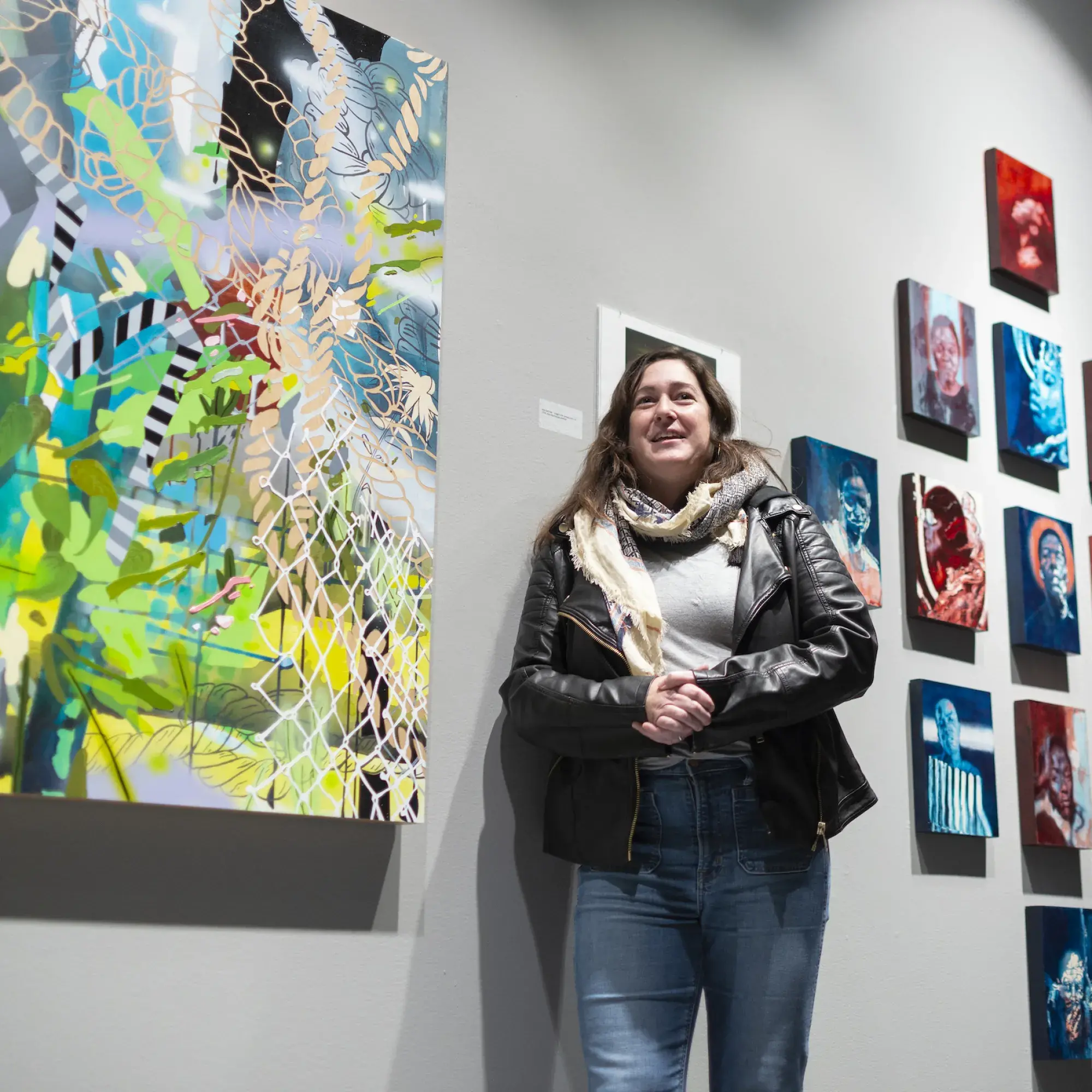 Woman wearing jeans and leather jacket standing in front of art exhibit