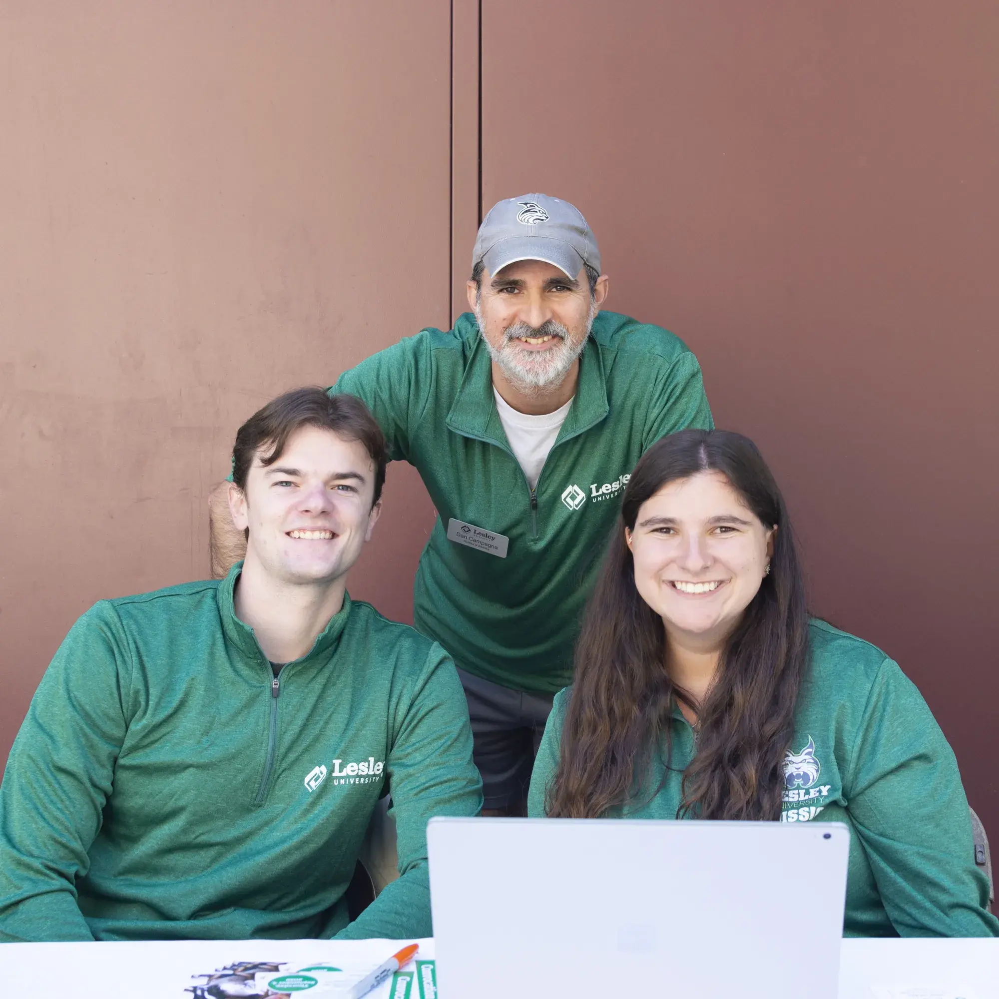 Three people posing in front of a laptop in green Lesley jackets