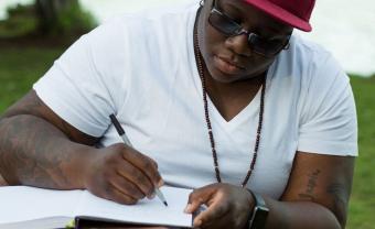 Aqueela Culbreath-Britt writing outside in a sunny park.