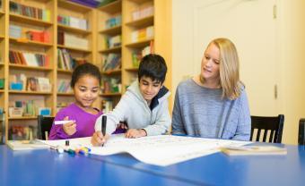 teacher Ellie Brennan sitting at table with 2 children