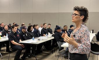 Gina standing up giving a training to people sitting at long white tables