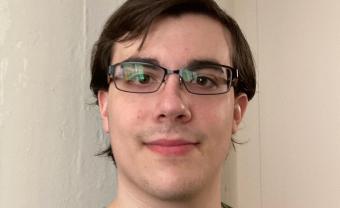 A photo of Matthew Stratoti. He is a white man with brown hair and brown eyes. He is wearing glasses and a green t-shirt.