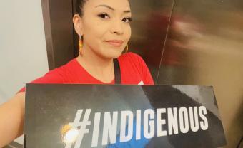Serene Thin Elk holding a sign that says "#INDIGENOUS"