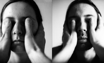 black and white photo of two people standing with another person's thumbs covering their eyes