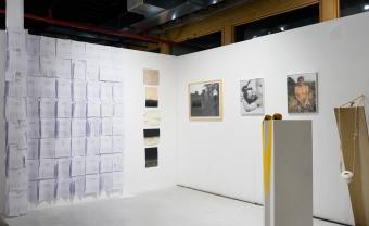 gallery exhibit with papers stuck to the white wall and framed images behind pedestals