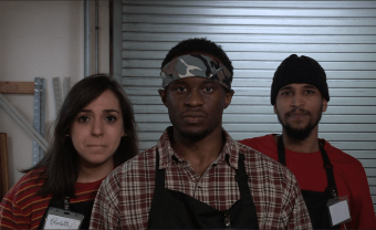 Three people wearing black aprons look into the camera 