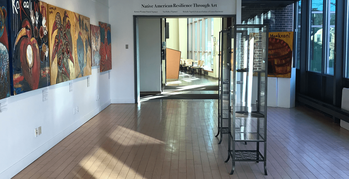 view of gallery space with sun light coming through on floor and paintings hanging on the wall