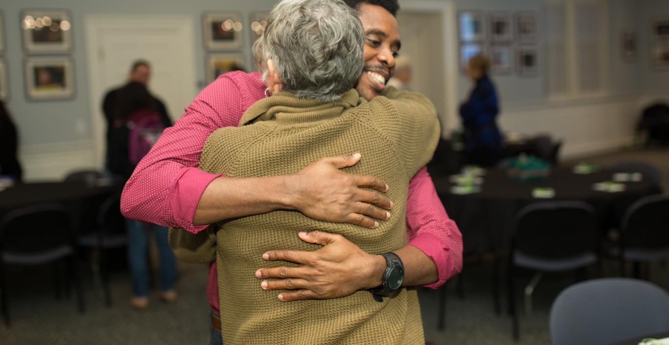 Student Lesly Precil in a pink shirt hugs professor Jan Wall in a mustard sweater.