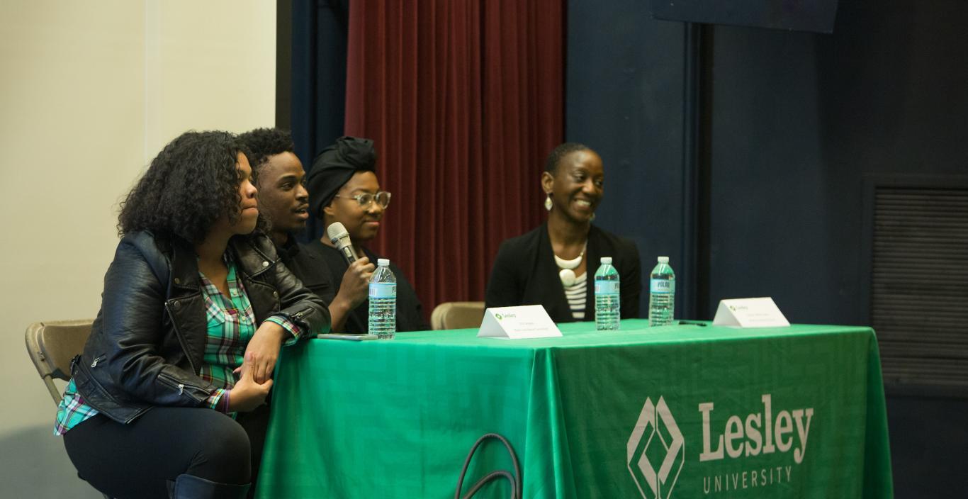 four people sitting at a Lesley University table, taking turns speaking into a microphone