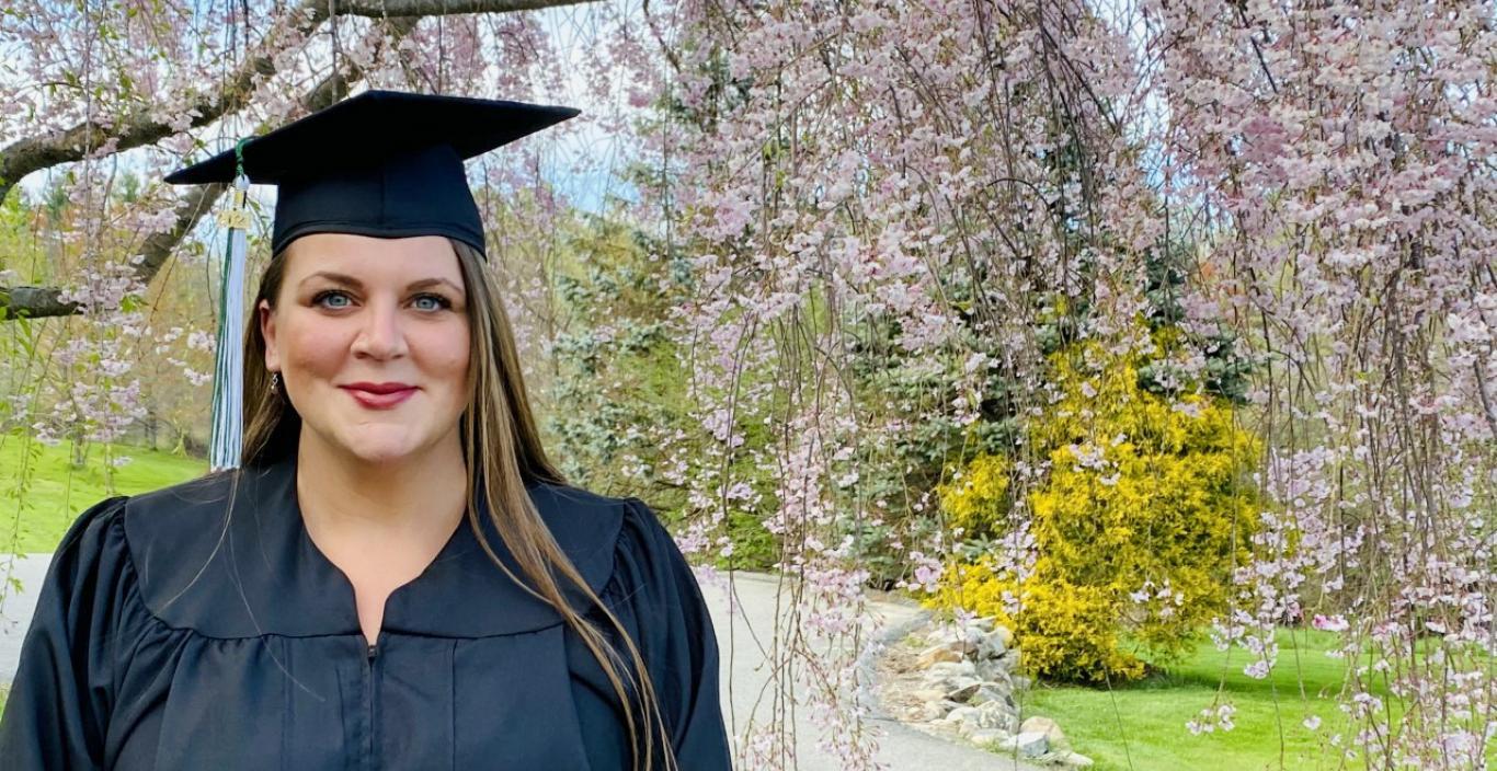 Alice Smith in graduation gown outside in front of blooming tree.