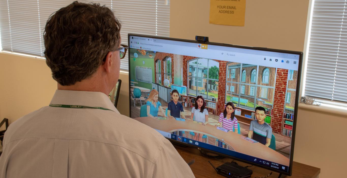 A man looks at a wide screen TV where the images of avatars are displayed.