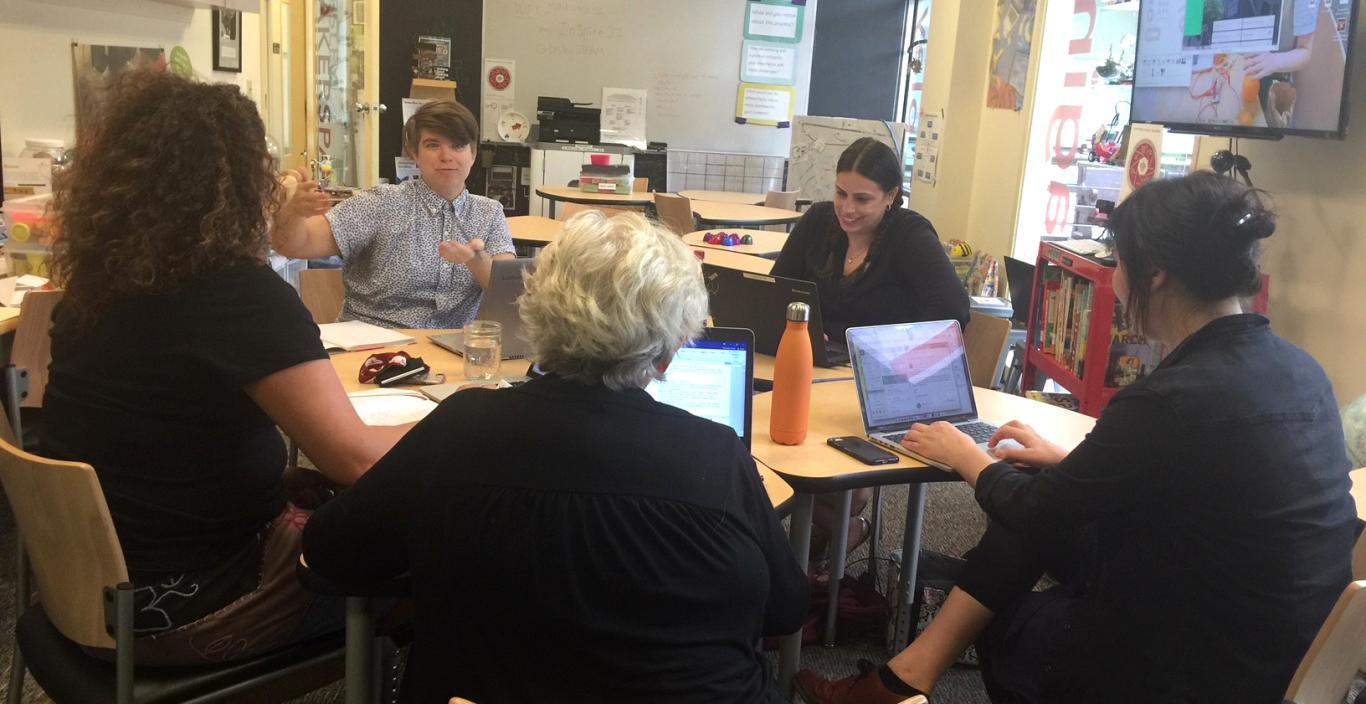 Lesley faculty members sitting around a round table in a classroom having a discussion.