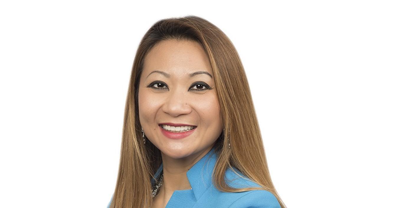 New trustee member Bopha Malone stands with her arms crossed in a blue suit.
