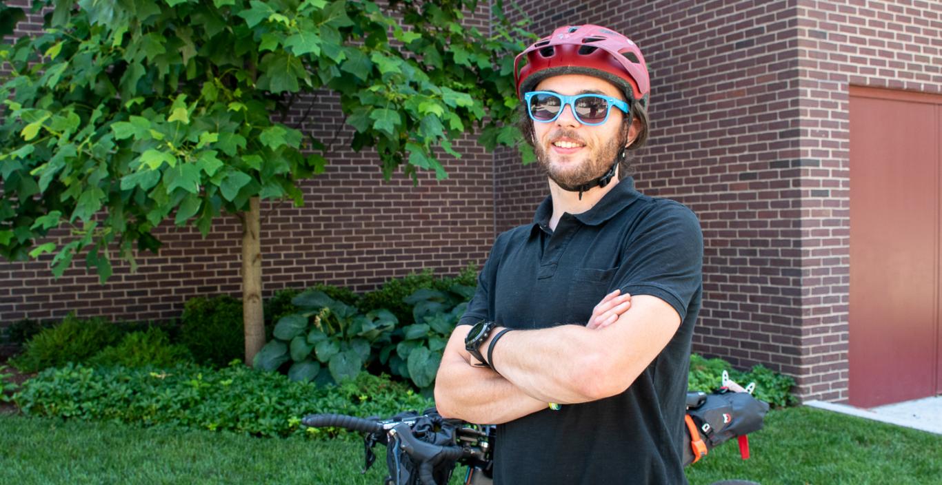 Brendan Walsh wearing his helmet and sunglasses, standing with arms crossed in front of bike.