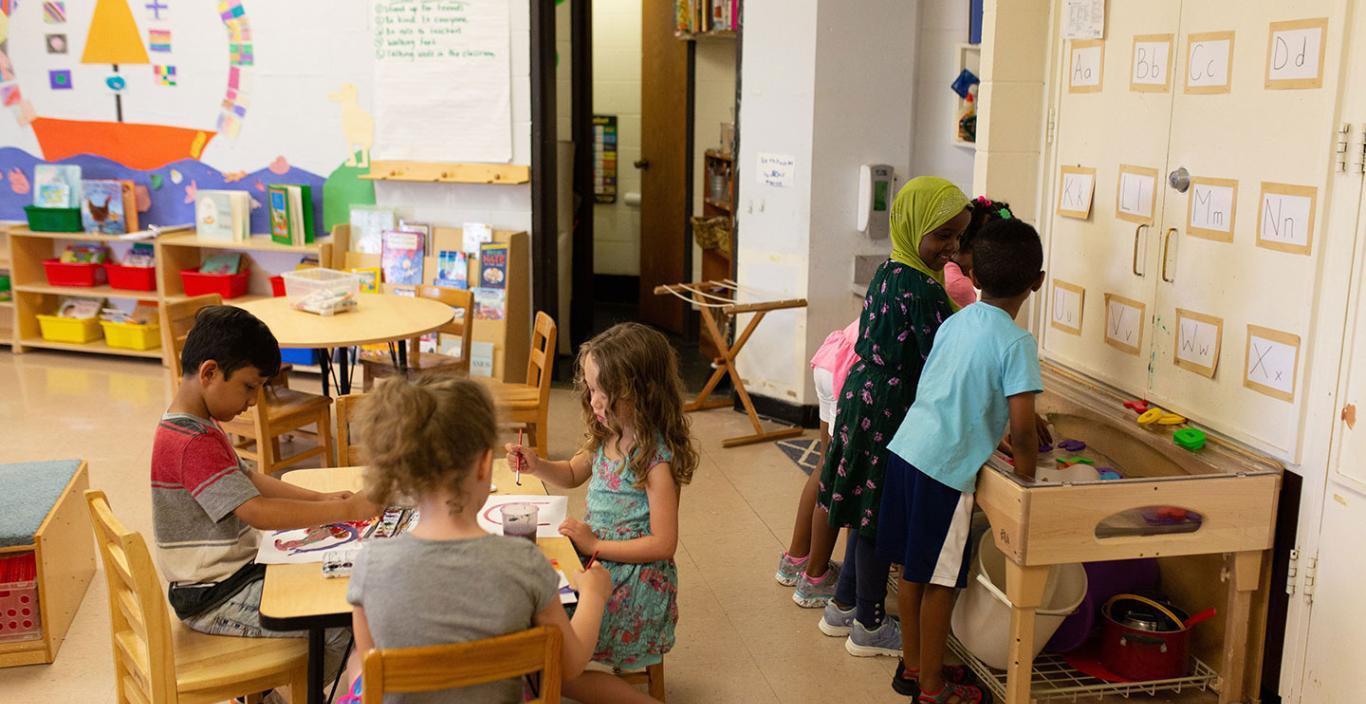 Young children paint and play at a sensory table in a classroom