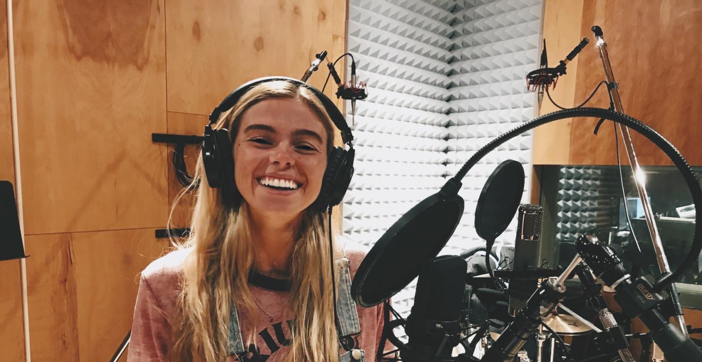 Carly Eaton in a music studio with headphones on standing in front of a mic