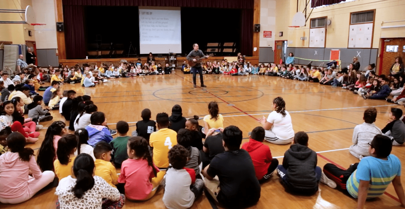 David Levine plays the guitar in front of a group of children