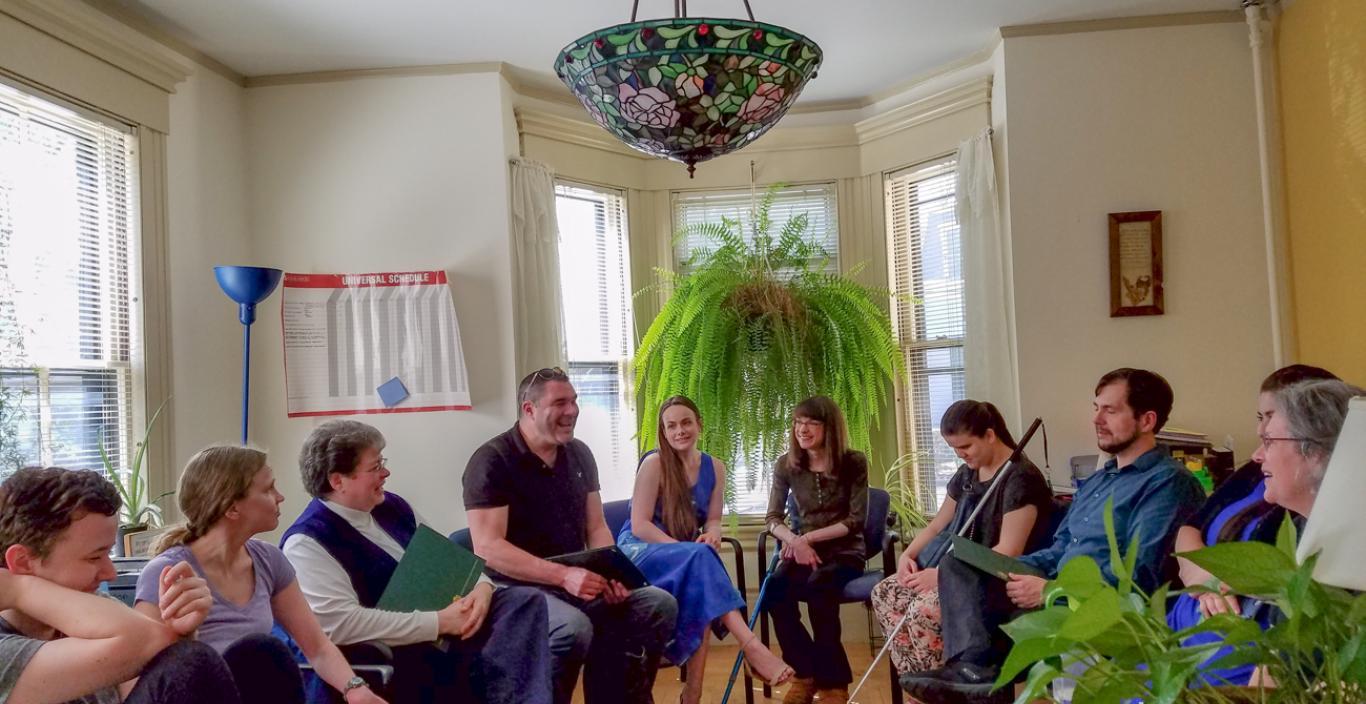 A group of peple sit in a circle in a room.
