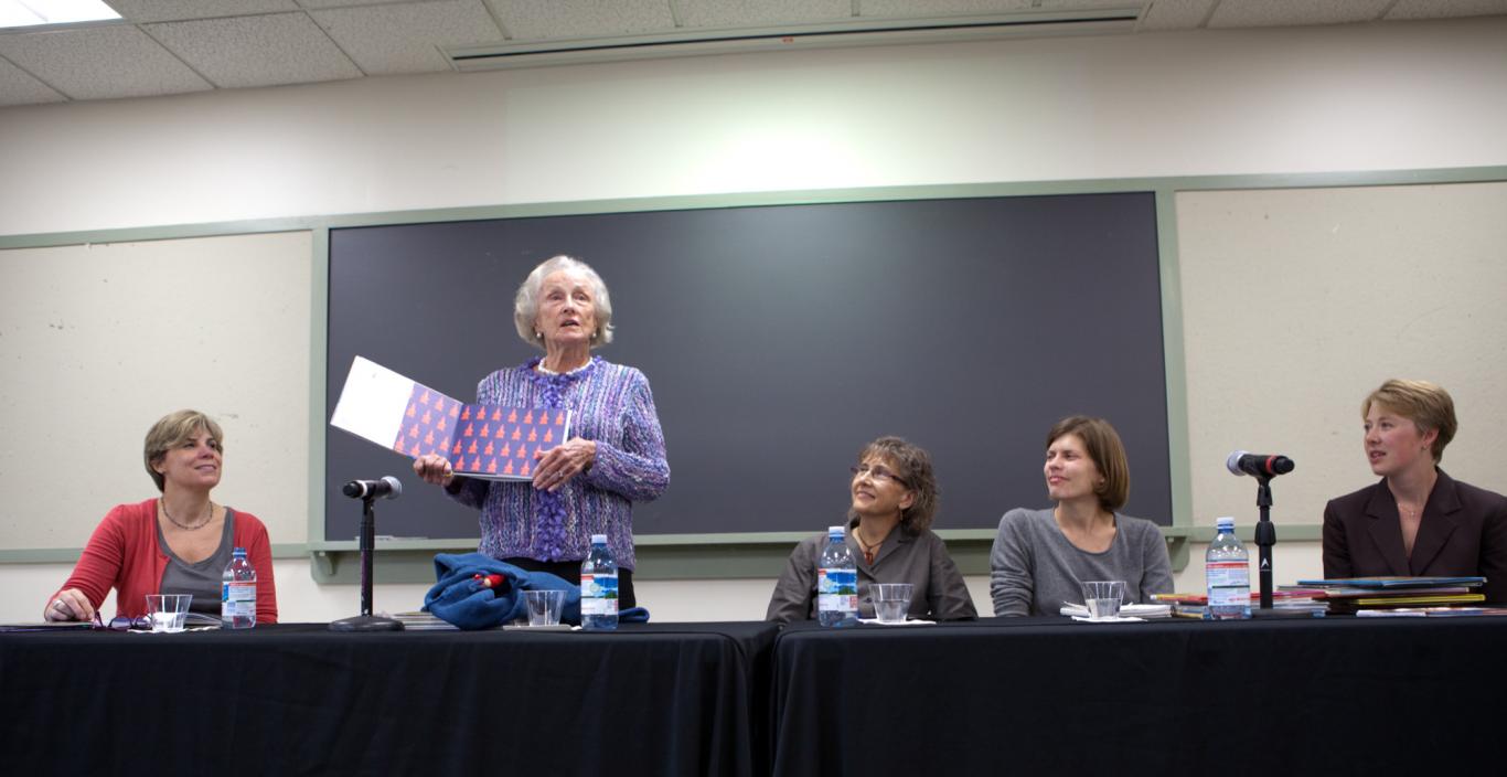 Evelyn Finnegan in 2011 holding a picture book and standing at a table with a panel of people